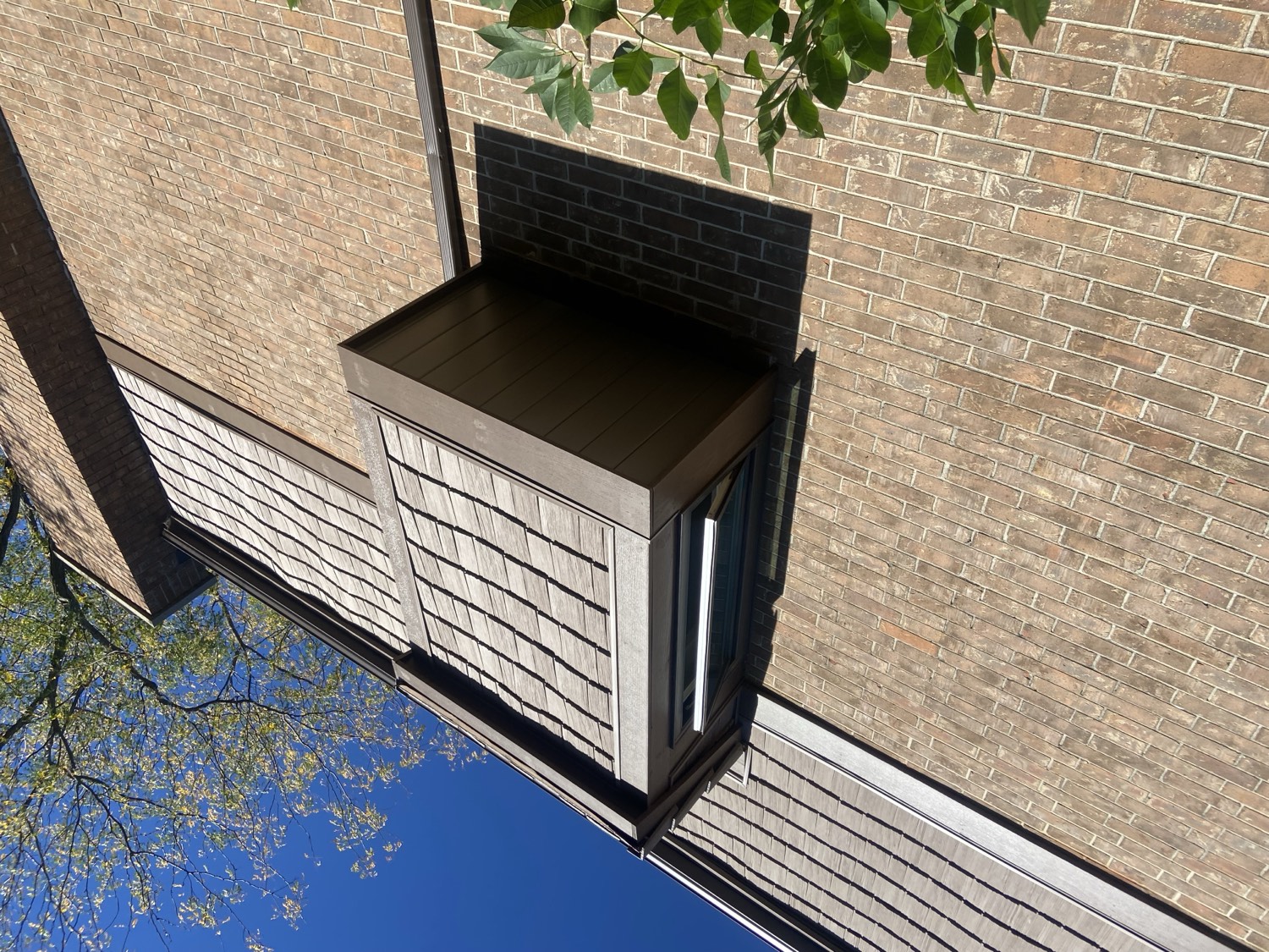 Exterior detail of brick and cedar-shake siding against a clear sky